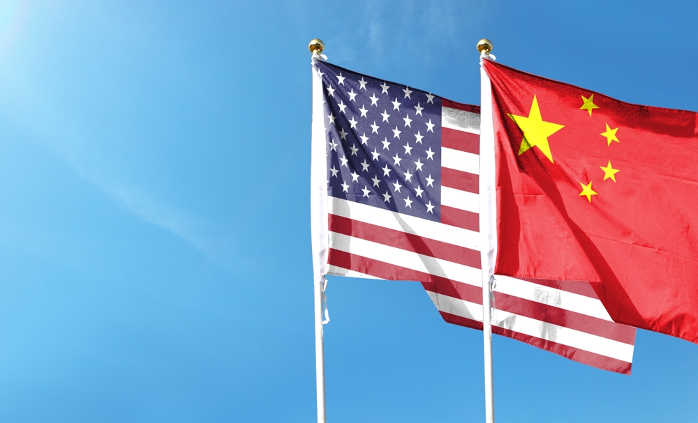 Image of the American flag and Chinese flag against a cloudy sky, representing the US & China trade agreement.